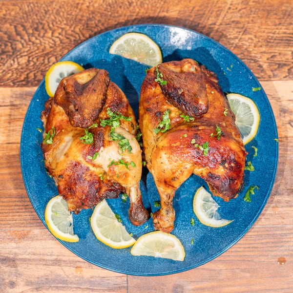 Two whole roasted chickens, garnished with parsley and lemon slices, on a blue plate.