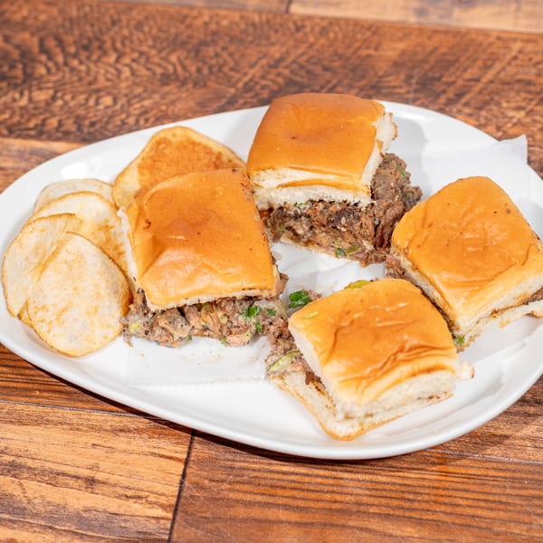 Four sliders with savory filling and a side of potato chips on a white plate.