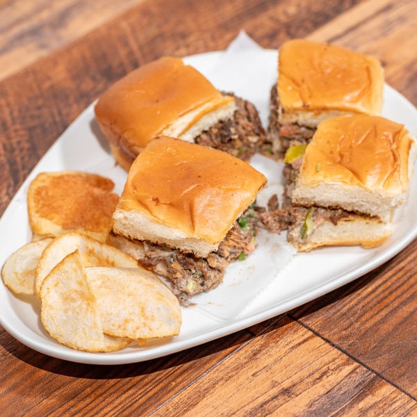 Four sliders with savory filling and a side of potato chips on a white plate.