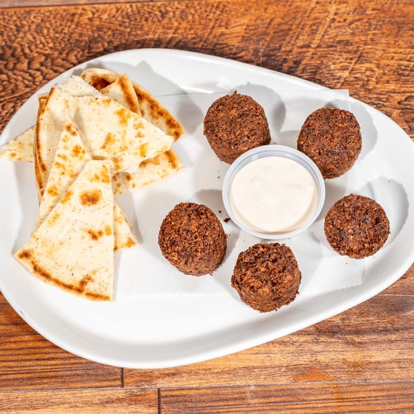 A white plate with falafel, pita bread triangles, and a small cup of white dipping sauce.