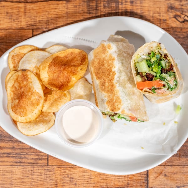 A falafel wrap, cut in half, with a side of potato chips and dipping sauce on a white plate.