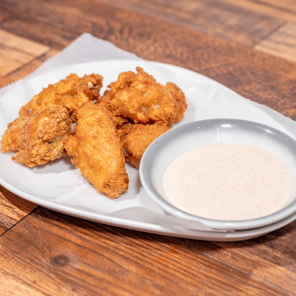 Crispy fried chicken wings on a white plate with a side of creamy pink dipping sauce.