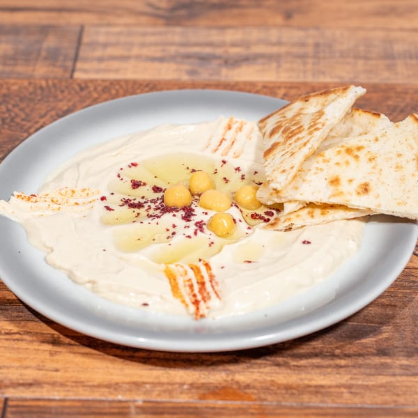 Creamy hummus drizzled with olive oil, chickpeas, and red spice, served with pita bread.