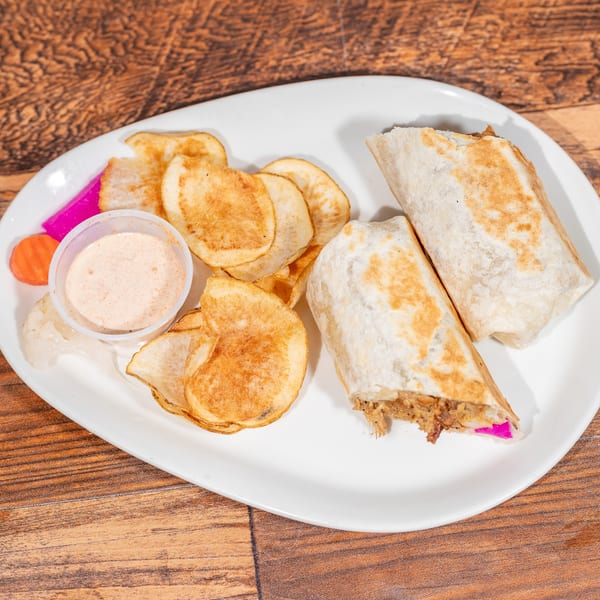 Two shawarma wraps with a side of chips, sauce, and pickled vegetables on a white plate.