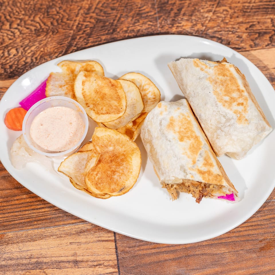 Two shawarma wraps with a side of chips, sauce, and pickled vegetables on a white plate.