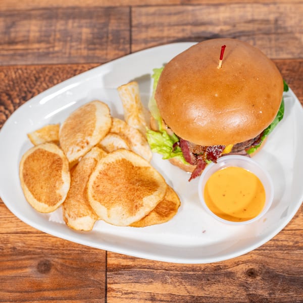 A burger with bacon, lettuce, and cheese, served with potato chips and a side of dipping sauce.