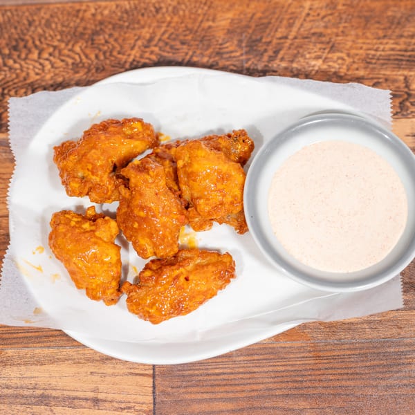 A plate of six orange-glazed chicken wings with a side of creamy dipping sauce on a wooden table.