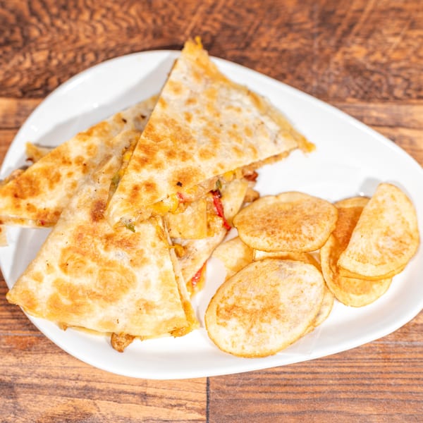 Golden-brown quesadilla triangles with melted cheese and vegetables, served with potato chips on a white plate.