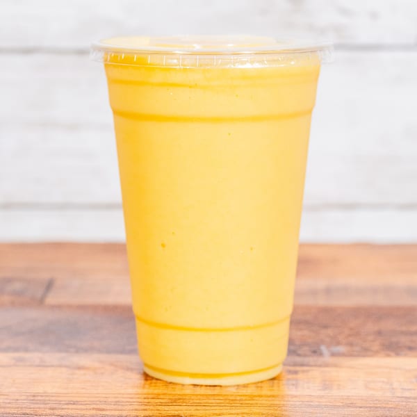 A vibrant yellow smoothie in a clear plastic cup with a lid, on a wooden table.